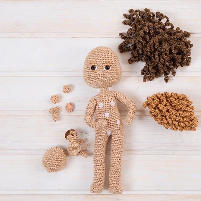 Identidad de sexo. Muñecas personalizables: creatividad, identidad y conexión emocional. La imagen muestra el proceso artesanal y personalizado de creación de una muñeca de crochet. Sobre una base de madera clara, se observa un cuerpo tejido a mano con varios puntos de velcro estratégicamente colocados que permiten fijar diferentes partes del cuerpo, rostros, orejas y cabellos intercambiables. A su alrededor se disponen piezas adicionales como mechones de lana rizada en distintos tonos de marrón, pequeñas orejas, bocas y cabecitas secundarias. Esta composición refleja el alma de un trabajo hecho con amor, donde cada detalle puede adaptarse para representar a una persona real. Estas muñecas terapéuticas ofrecen no solo compañía, sino también identidad, inclusión y posibilidades infinitas de personalización para conectar emocionalmente con quienes más lo necesitan. Propiedad de Mikadoll